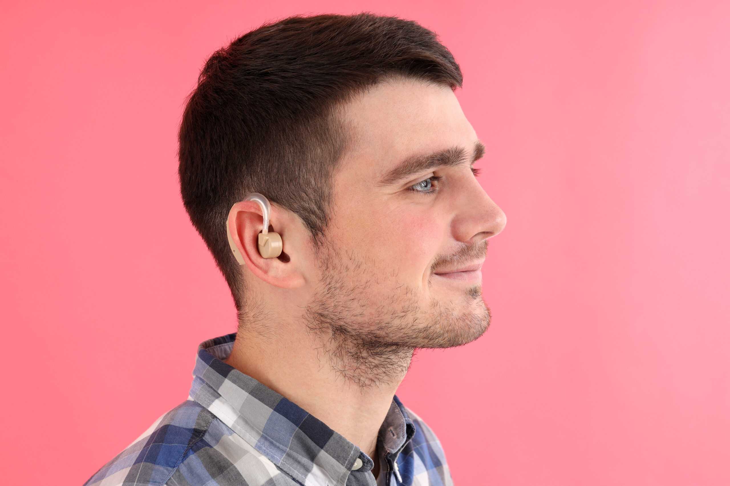 young man with hearing aid pink background scaled