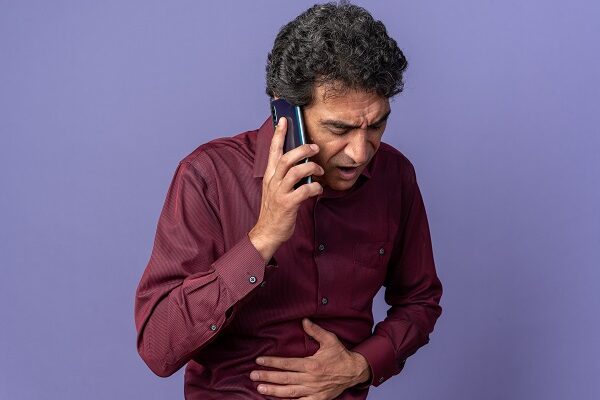 senior man purple shirt looking unwell touching his belly while talking mobile phone